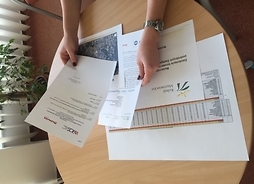 Ilustracja przedstawia zdjęcie rąk trzymających dokumenty z logo Kolei Mazowieckich