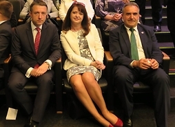 Troje polityków siedzących na trybunach w sali plenarnej