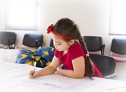 Dziewczynka przy szkolnym stole pisze długopisem w zeszycie
