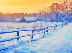 zimowy krajobraz wiejski - przykryte śniegiem polna droga, płot, chata w oddali, niebo pomarańczowe od zachodzącego słońca