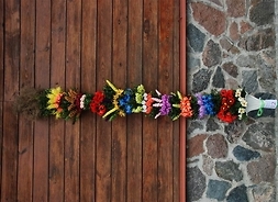 Palma wykonana przez KGW Łęczanki, w której dominują kolorowe kwiaty i kłosy zbóż zrobione z bibuły. Palma ustawiona pionowo.