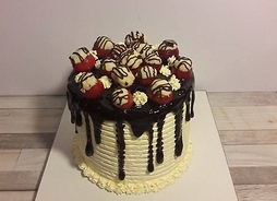 biały tort oblany ciemną czekoladą na wierzchy praliny