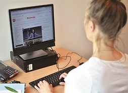 Kobieta siedząca przed biurkiem, na którym stoi komputer i telefon