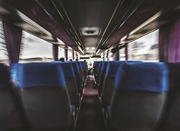 Wnętrze pustego autobusu pokazujące rzędy foteli od tyłu w stronę przedniej szyby