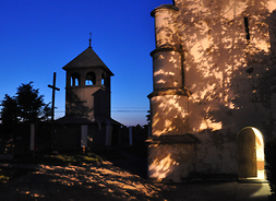 oświetlona część budynku kościoła, na drugim planie dzwonnica