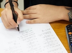 Zeszyt do matematyki z rozwiązywanymi zadaniami, ręka dziewczęca z zegarkiem i fragment kalkulatora matematycznego