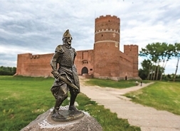 Metalowa figura rycerza w tle zamek z cegły