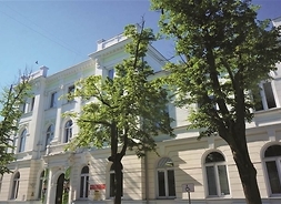 Zdjęcia przedstawia fasadę budynku książnicy, przed którym rosną dwa drzewa