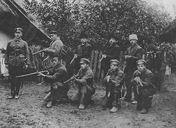 Grupa ośmiu chłopców z karabinami i dowódca, ubranych w różne, samodzielnie kompletowane umundurowanie
