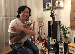 Muzyk z psem chihuahua na rękach w domu, w tle gitary i złote płyty na ścianie