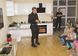 Szkolenia dla najmłodszych. Strażak stoi modelową kuchnią, przed nim siedzą dzieci