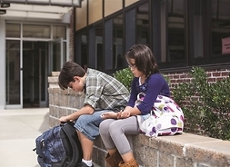 przed budynkiem szkoły na murku siedzi dwoje uczniów