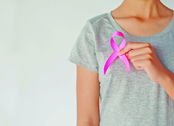 Kobieta trzyma w ręku wstążkę symbolizującą raka piersi