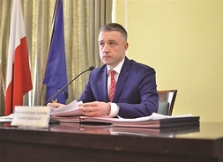 Zdjęcie przedstawia przewodniczącego sejmiku Ludiwka Rakowskiego, który siedzy za prezydialnym stołem, w ręku trzyma dokumenty