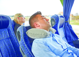 Mężczyzna siedzi na fotelu w autokarze, śpi, pod głową na poduszkę podróżną