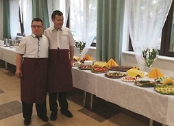 dwaj mężczyźni stoją obok stołu z cateringiem