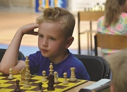 skoncentrowany chłopiec patrzy na pionki ustawione na szachownicy