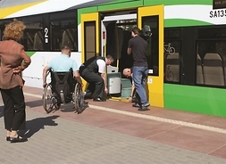 na peronie stoi pociąg, przy pomocy pracowników kolei na wózku wjeżdża do niego niepełnosprawny, nagrywa to kamerzysta