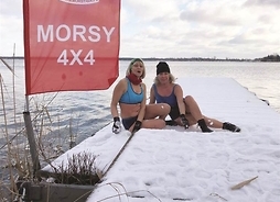 na molo pokrytym śniegiem w strojach kąpielowych siedzą dwie kobiety