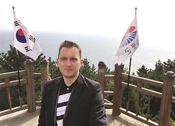 mężczyzna stoi nad brzegiem morza w tle dwie flagi koreańskie