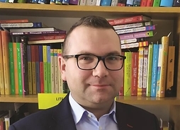 Zdjęcie prtetowe psychologa Łukasza Smółki na tle półek z książkami
