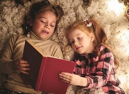 Chłopiec i dziewczynka leżą na miękkim kocu i czytają książkę