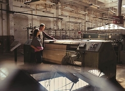 wnętrze fabryki lnu, maszynom przygląda się kobieta i mężczyzna