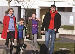 rodzice z dwojgiem dzieci i dwoma psami spacerują między budynkami