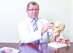 profesor siedzi przy biurku i pokazuje na modelu czaszki ludzkiej obszar
