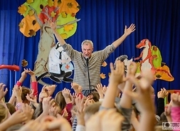 Mężczyzna z uniesionymi do góry rękoma, podczas zabawy z dziećmi. Dzieci odwrócone tyłem do patrzącego również mają uniesione ręce