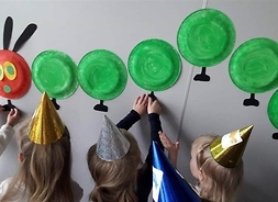 Dzieci przyklejają na ścianie gąsiennicę zrobioną z papieru