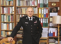 Ryszard Nowaczewski w mundurze strażaka, stoi na tle regałów z książkami w swoim miejscu pracy.