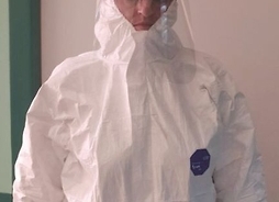 Jadwiga Gryziewska, oddziałowa SOR ze szpitala bródnowskiego stoi na tle ściany, ubrana w kompletny strój ochronny przeciwepidemiczny.