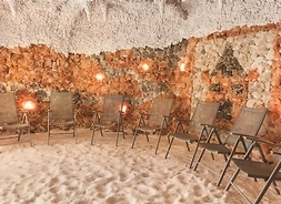 Wnętrze groty solnej. Ściany ułożone z dużych brył soli, na podłodze wysypana drobna sól. Pod ścianami stoją krzesła dla kuracjuszy.