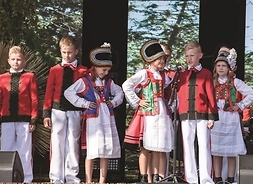 Grupa dzieci w strojach regionalnych podczas występu na scenie.