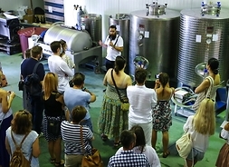 grupa ludzi stoi w p[omieszczeniu z maszynami do produkcji wina