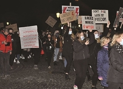 Grupa osób z plakatami z hasłami strajkowymi idzie ulicą