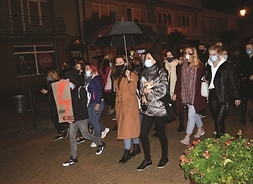 Grupa kobiet z hasłami strajkowymi i rozłozonymi parasolkami idzie ulicą