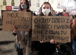 Dwie młode kobiety trzymają w rękach hasła protestacyjne wypisane na kartonowych płachtach
