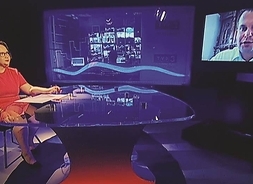 zdjęcie z planu telewizyjnego programu publicystycznego, widok na kobietę przy biurku, w drugim oknie mężczyzna
