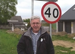 mężczyzna pozuje do zdjęcia na tle znaku z nazwą miejscowości