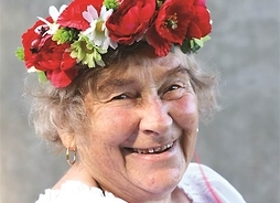 z wiankiem na głowie do zdjęcia pozuje starsza uśmiechnięta kobieta
