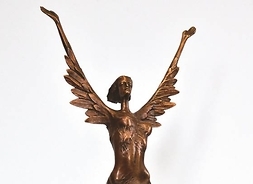 Statuetka przedstawiająca kobietę z uniesionymi do góry rękoma. Z jej ramion wyrastają pióra