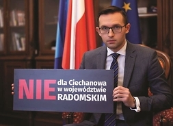 Mężczyzna w garniturze siedzi i trzyma tabliczkę z napisem nie dla ciechanowa w województwie radomskim