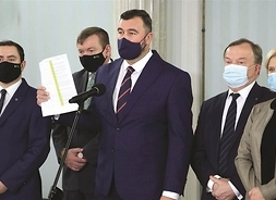 Mariusz Bieniek, starosta płocki pokazuje dokument, który trzyma w ręku. Za nim stoi grupa samorządowców i parlamentarzystów. Wszyscy w maskach ochronnych.