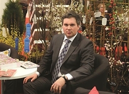 Mężczyzna w garniturze siedzący na stoisku wystawienniczym, wśród roślin