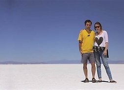Młody mężczyzna i młoda kobieta stoją blisko siebie na plaży lub pustyni. Nad nimi i piaskiem jest bezchmurne pogodne niebo
