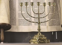 Siedmioramienny świecznik żydowski stoi na tle rozwinietego zwoju Tory