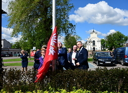 grupa  ludzi wciąga flagę województwa mazowieckiego na maszt