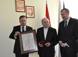 powiększ: od lewej marszałęk Adam Struzik trzyma oprawiony w ramę dyplom, ks. tadeusz Tomasiński trzyma medal